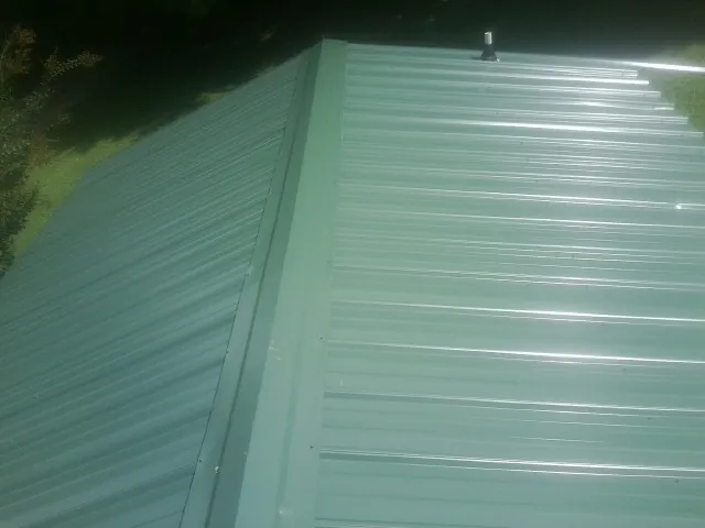 New green metal panels meeting at the ridge of a roof — Flat Roof Repair work by our crew in Annville
