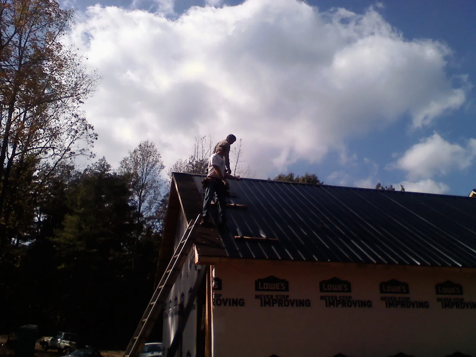 Roofer fastening dark metal panels high against a cloudy sky, from a Roof Inspection job in Annville
