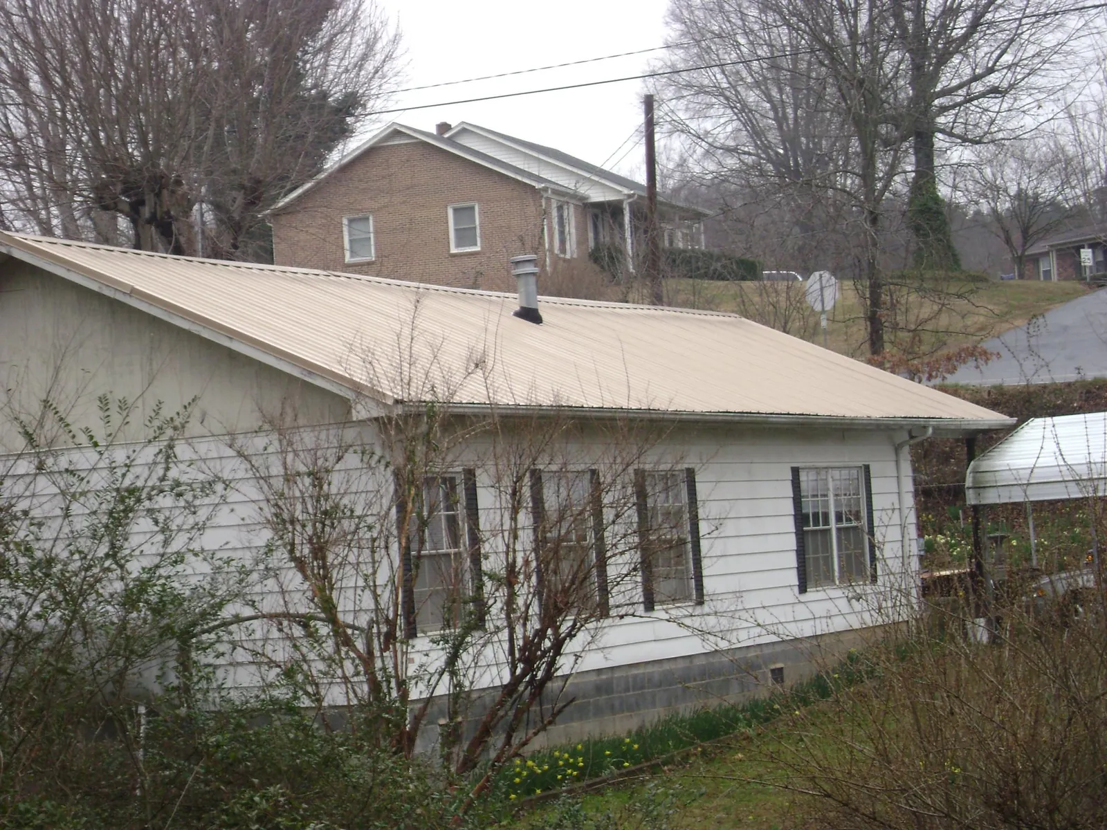 Tan metal roof on a white sided house set into a hillside — Commercial Roofing by Roofing Brothers in Annville